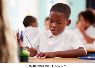 Male Elementary School Pupil Wearing Uniform Working At Desk