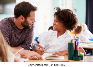 Male Elementary School Teacher Giving Female Pupil Wearing Uniform One To One Support In Classroom