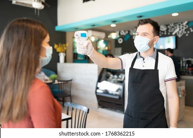 Male Employee Checking Body Temperature Of Young Woman Through Thermal Scanner In Restaurant