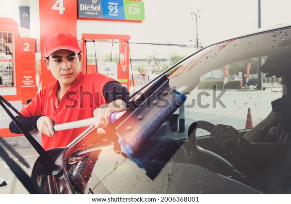 Male employee is committed to cleaning wiper\
blades and windshields while customers sit and wait to refuel at a\
gas station : Excellent customer service work of male staff in a\
modern gas station\
