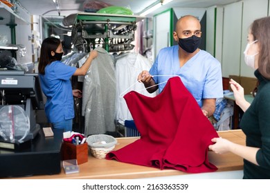 Male Employee In Protective Mask With Client In Modern Laundry, Returning Clothing After Dry Cleaning