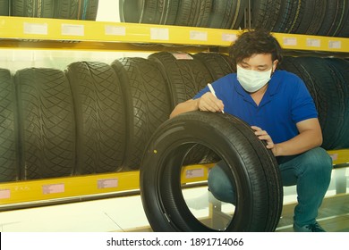 Male Employee Wearing A COVID-19 Mask In A Car Showroom Chooses To Inspect New Tires And Check The Number And Size Series For Customers Who Visit The Showroom : Quality And Standardized Tire Business
