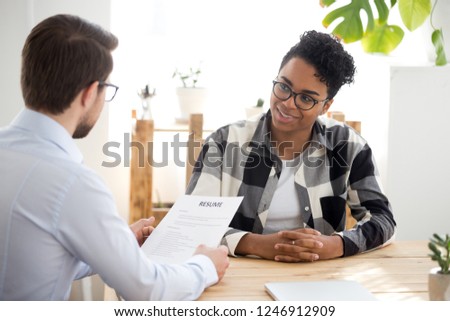 Male employer holding resume talking with African American female job candidate at interview, black millennial girl recruitment process, speak with HR manager, businessman consider applicant cv