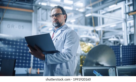 Male Engineer Confident And Focused Thinking, Working On Laptop At Aerospace Satellite Manufacturing Facility. Top World Scientists Doing Science And Technology Research In Space Program