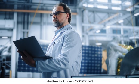 Male Engineer Confident And Focused Thinking, Working On Laptop At Aerospace Satellite Manufacturing Facility. Top World Scientists Doing Science And Technology Research In Space Program