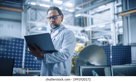 Male Engineer Confident And Focused Thinking, Working On Laptop At Aerospace Satellite Manufacturing Facility. Top World Scientists Doing Science And Technology Research In Space Program