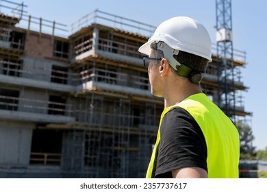 Male engineer at the construction site of a building during an inspection. Man supervisor, professional architect wearing hard hat safety helmet and reflective clothing vest. - Shutterstock ID 2357737617