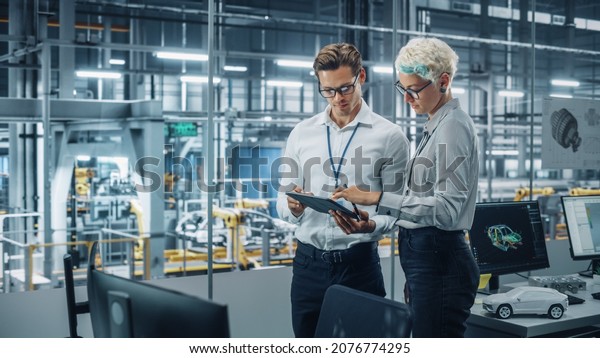 Male\
Engineer and Female Industrial Product Designer Discuss Work while\
Standing in Office at a Car Assembly Plant. Industrial Specialists\
Working on Vehicle Design in Technological\
Factory.