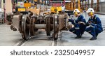 Male engineer and female maintenance staff in uniform looking at electric train parts for repairing electric train in electric train depot factory.
