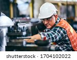 Male engineer metalworker industrial experienced operator technician worker in safety hard helmet working on lathe machine, professional man in industry technology manufacturing factory workshop