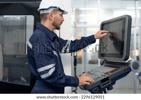 Male engineer operating cnc machine in control panel at factory. Smiling man technician in uniform and helmet safety working at workshop heavy metal industrial