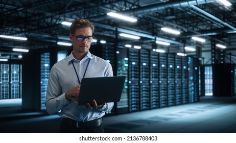 Male Engineer Programs Something and Holding Laptop Computer while Works in a Dark Modern High-Tech Office. High-Speed Data Transfer and Smooth Server Operation, Analytics, Statistics Concept