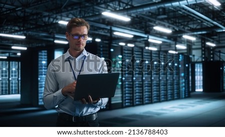 Male Engineer Programs Something and Holding Laptop Computer while Works in a Dark Modern High-Tech Office. High-Speed Data Transfer and Smooth Server Operation, Analytics, Statistics Concept