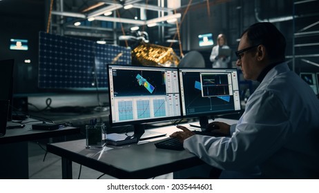 Male Engineer Uses Computer While Working On Satellite Construction. Aerospace Agency: Scientist Is Using Computer Software For Programming And Assembly Of Spacecraft For Space Exploration Mission.