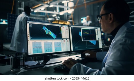 Male Engineer Uses Computer while Working on Satellite Construction. Aerospace Agency: Scientist is Using Computer Software for Programming and Assembly of Spacecraft for Space Exploration Mission.