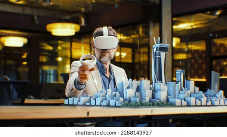 Male engineer uses VR headset and wireless controllers, creates architectural project of the city in virtual reality. Man works in modern hi-tech company. 3D hologram. Future digital AI technologies. - Powered by Shutterstock