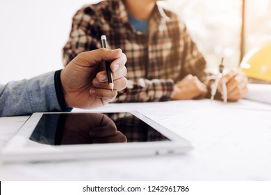 Male engineering using digital tablet with architectural plan on desk.