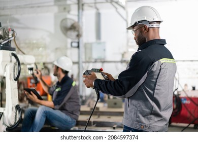 Male engineers control robot arm machine welding steel with remote control in factory workshop. - Powered by Shutterstock