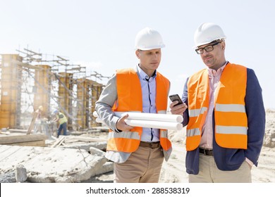 Male engineers using mobile phone at construction site against clear sky