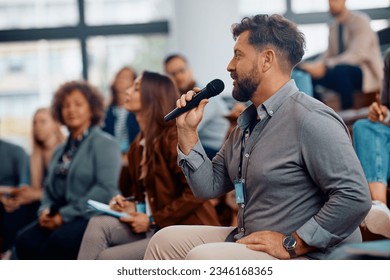 Male entrepreneur asking a question while attending business seminar in conference hall.