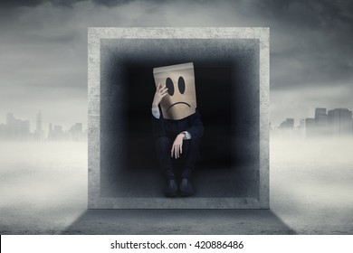 Male Entrepreneur With Cardboard Head Looks Confused And Sitting Inside A Box Outdoors