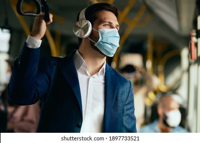 Male entrepreneur listening music over headphones and wearing face mask while commuting by bus during coronavirus pandemic. - Powered by Shutterstock