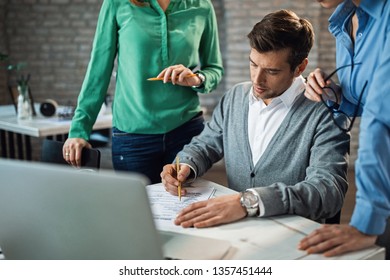 Male entrepreneur is signing a contract in presence of two female colleagues in the office.  - Powered by Shutterstock