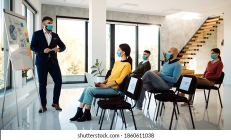 Male Entrepreneur Talking To Group Of People During A Business Seminar In Board Room. All Of Them Are Wearing Face Masks Due To COVID-19 Pandemic. 