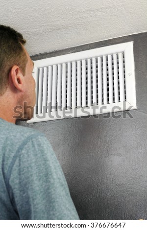 Male examines an indoor air duct register for dirt to understand if he should get it cleaned. One guy in his forties peers into and inspects a furnace central heating vent.