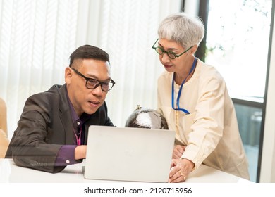 Male Executive Looks At Sales Targets On A Laptop With A Senior Female Manager Employee At A Desk In The Executive Office. 