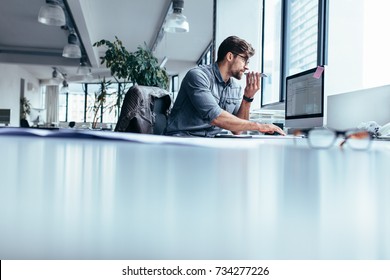Male executive working on computer and talking on mobile phone. Businessman working in office with phone. - Shutterstock ID 734277226