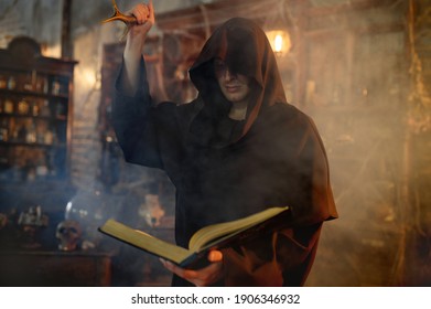 Male exorcist in black hood holds book of spells - Shutterstock ID 1906346932