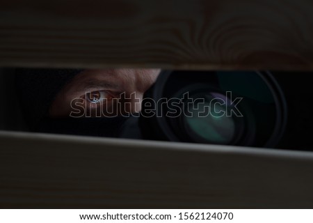 Male eye and camera close-up. Recording to a hidden camera. Private detective with camera looks at a cleft. Espionage background. The concept of eavesdropping, espionage, gossip and the yellow press