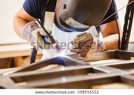 Male in face mask welds with argon-arc welding