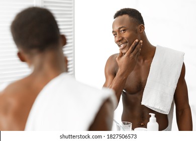 Male Facial Skincare. Attractive Muscular Black Guy Touching Smooth Well-Shaved Face Looking In Mirror Standing Shirtless In Modern Bathroom Indoor. Male Beauty Routine, Care For Skin After Shaving