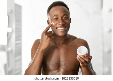 Male Facial Skincare. Cheerful African Guy Applying Cream On Face Holding Moisturizer Jar, Smiling To Camera Standing Shirtless Near Mirror In Bathroom At Home. Male Skin Care And Beauty Concept - Powered by Shutterstock