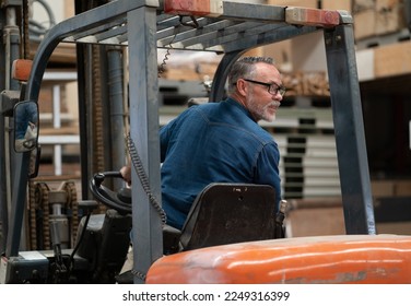 Male factory manager working in warehouse driving forklift truck. Portrait of forklift driver employee transporting merchandise in storehouse delivering to shelf. Industrial worker in industry vehicle - Powered by Shutterstock