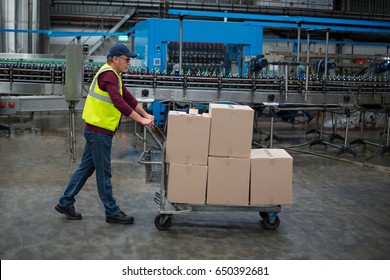 Male factory worker pulling trolley of cardboard boxes at drinks production factory - Powered by Shutterstock