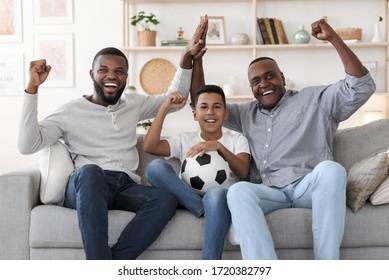 Male Family Leisure. Excited African Dad, Son And Grandfather Watching Football On Tv And Emotionally Cheering With Raised Fists