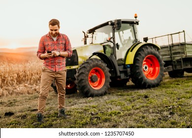 Male farmer working on field using smartphone in modern agriculture - tractor background - Powered by Shutterstock