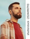 Male fashion concept. Portrait of proud charismatic active 30-year-old man posing over blue sky background. Perfect haircut and mustache. Hipster style. Low angle. Outdoor shot