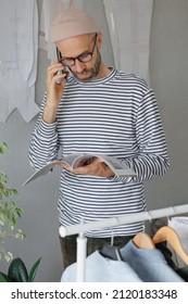 A Male Fashion Designer Or Fashion Designer Flips Through A Magazine And Talks On The Phone With A Client. An Adult Business Man Is Working In His Office. Senior Creative Director In A Striped Jacket