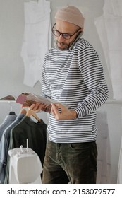 A Male Fashion Designer Or Fashion Designer Flips Through A Magazine And Talks On The Phone With A Client. An Adult Business Man Is Working In His Office. Senior Creative Director In A Striped Jacket