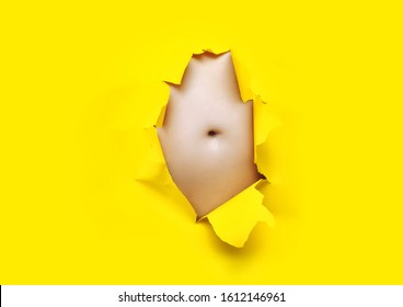 Male Fat, Flabby Stomach In A Torn Aperture Of Yellow Paper. The Concept Of Beer Belly, Gluttony And Cellulite. Copy Space.