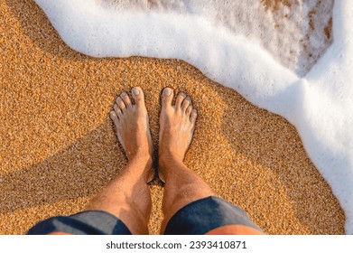 male feet barefoot on the waves of sea foam on a sandy golden beach on a summer day. top view of male legs in shorts and clear waters of the ocean - Powered by Shutterstock