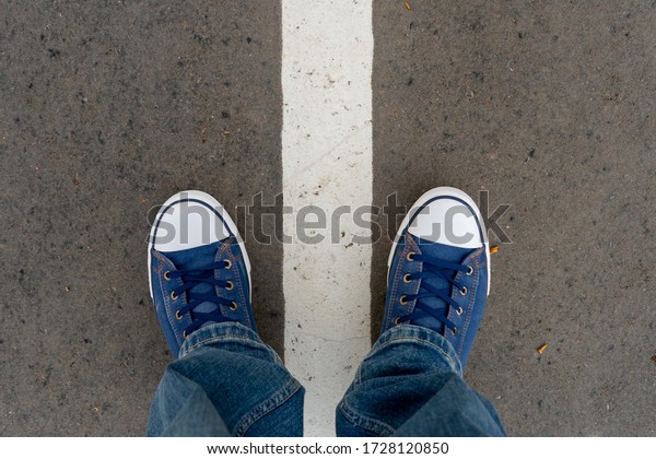 Male feet in blue jeans and\
blue sneakers shoes stand on street asphalt pavement with dividing\
line