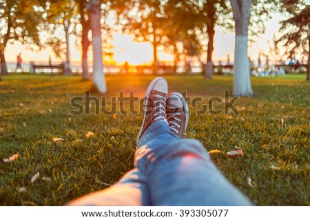 Male feet in gumshoes on green grass in the park at sunset