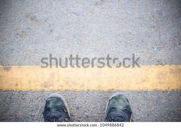Male feet and old black shoes standing on the\
concrete floor or street asphalt pavement with dividing line. Space\
for text and design