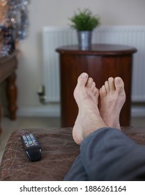 Male Feet Relaxing On The Sofa With Remote Control And Feet Up