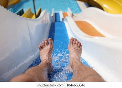 Male feet with splashing water on slide in water park. Entertainment in hotel pools and aquapark concept
